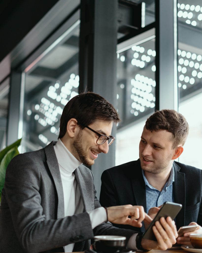 One-on-one meeting. Two young business people sitting at table in restaurant having a conversation using a phone and having a coffee. Businessman using a smartphone